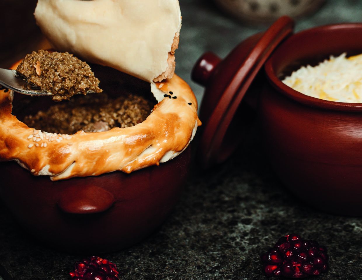 Haggis spooned from a pastry-topped pot beside neeps and tatties on a dark stone table