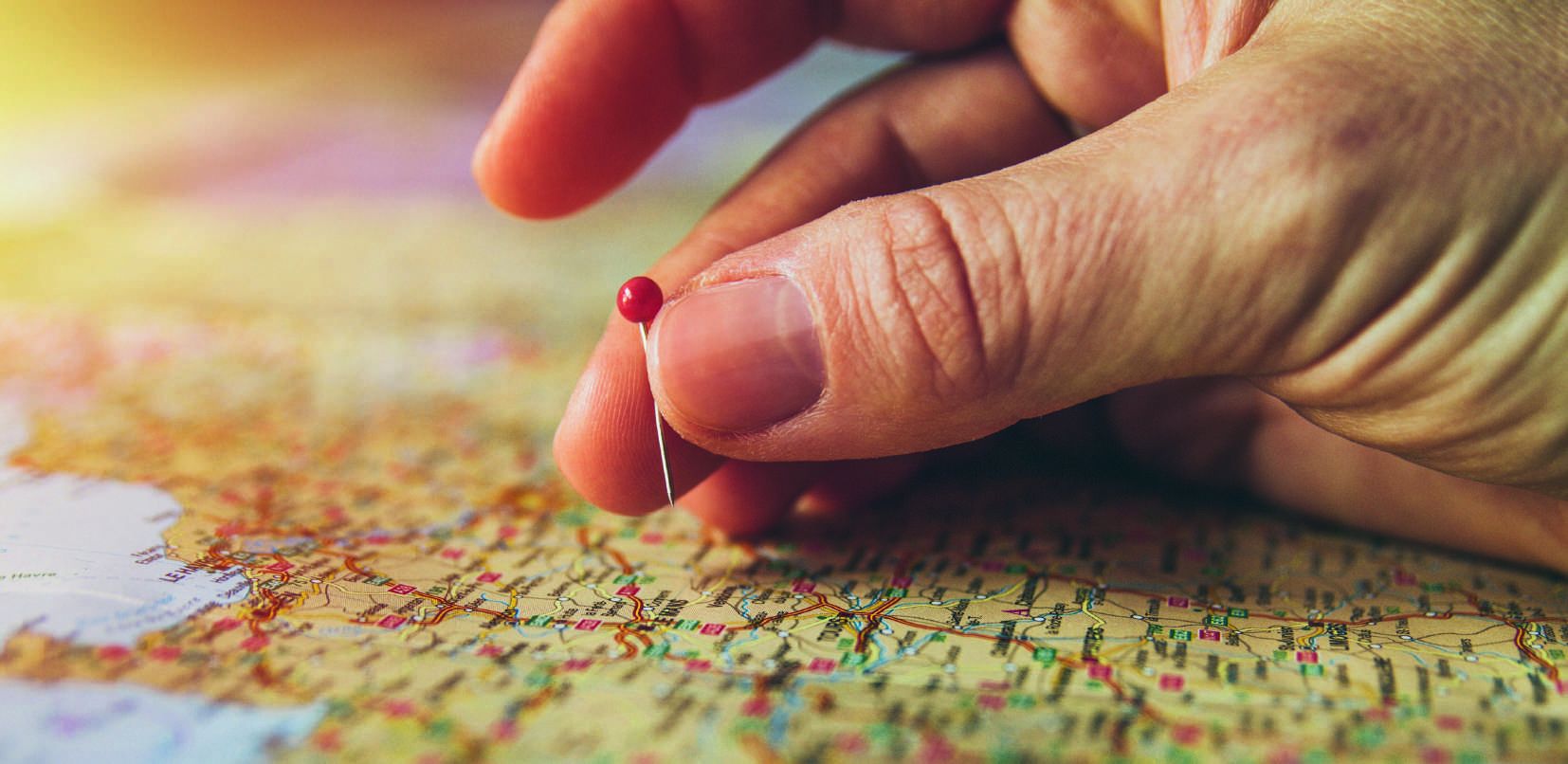 A hand placing a red pin into a folded road map, planning the route ahead